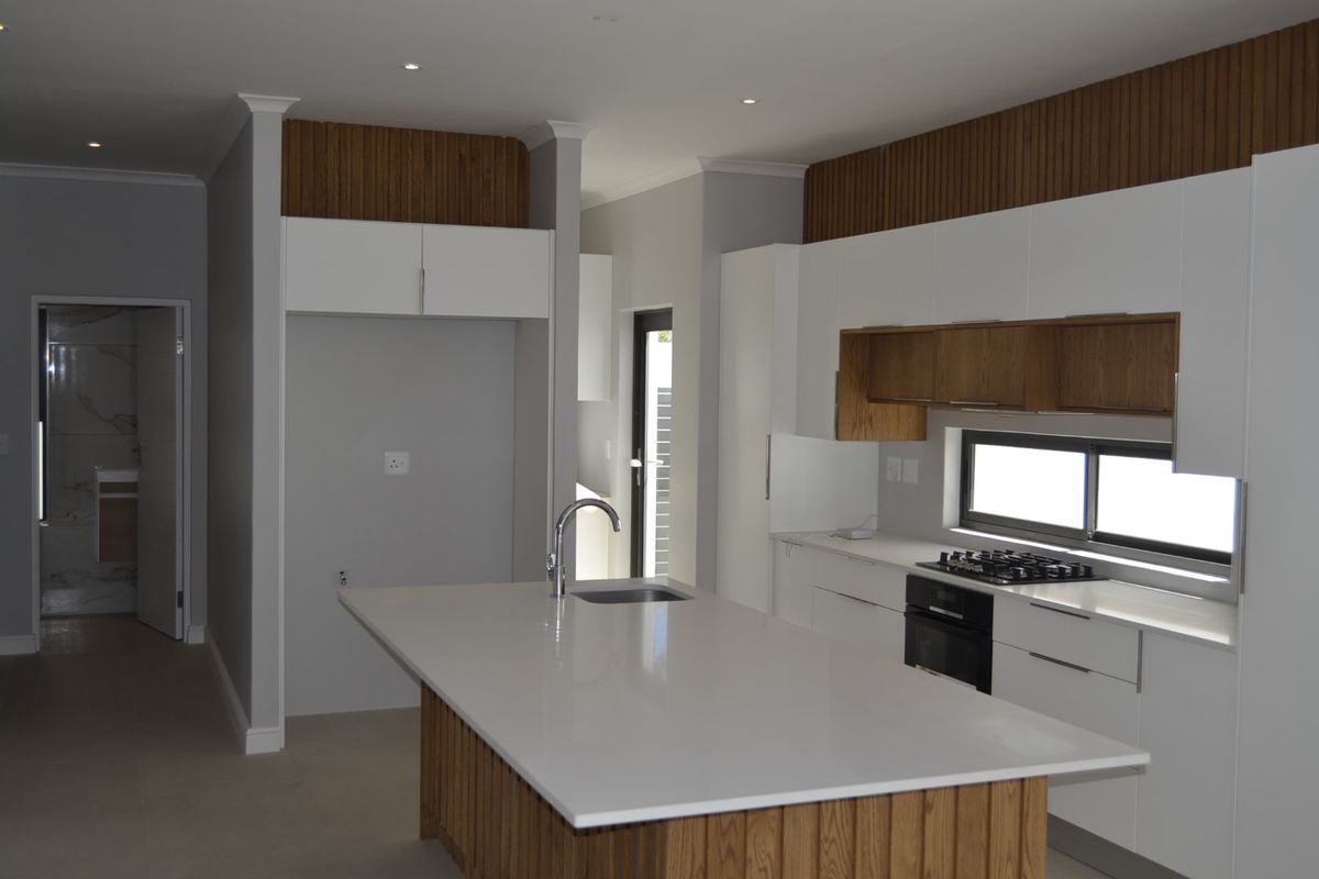 Modern kitchen featuring a central island with stone countertop, built-in oven, gas hob, and sleek white cabinetry with wood-panelled accents.