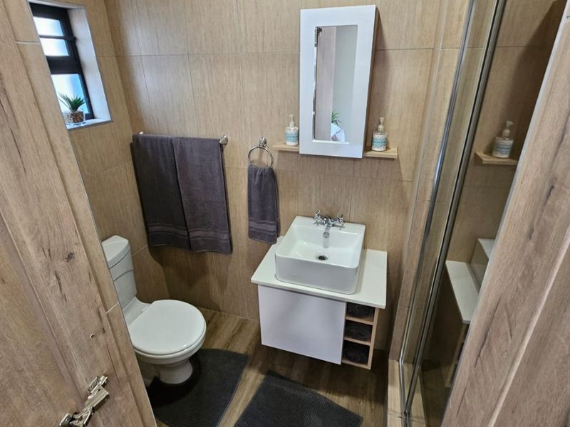 A modern, compact bathroom featuring wood-look wall and floor tiles, a wall-mounted vanity with a vessel sink, and a glass-enclosed shower.