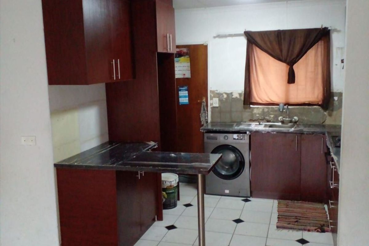 A dated kitchen featuring dark wood cabinetry, laminate countertops, and a breakfast bar, currently requiring cosmetic updates and wall finishing.