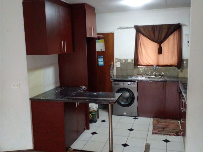 A dated kitchen featuring dark wood cabinetry, laminate countertops, and a breakfast bar, currently requiring cosmetic updates and wall finishing.
