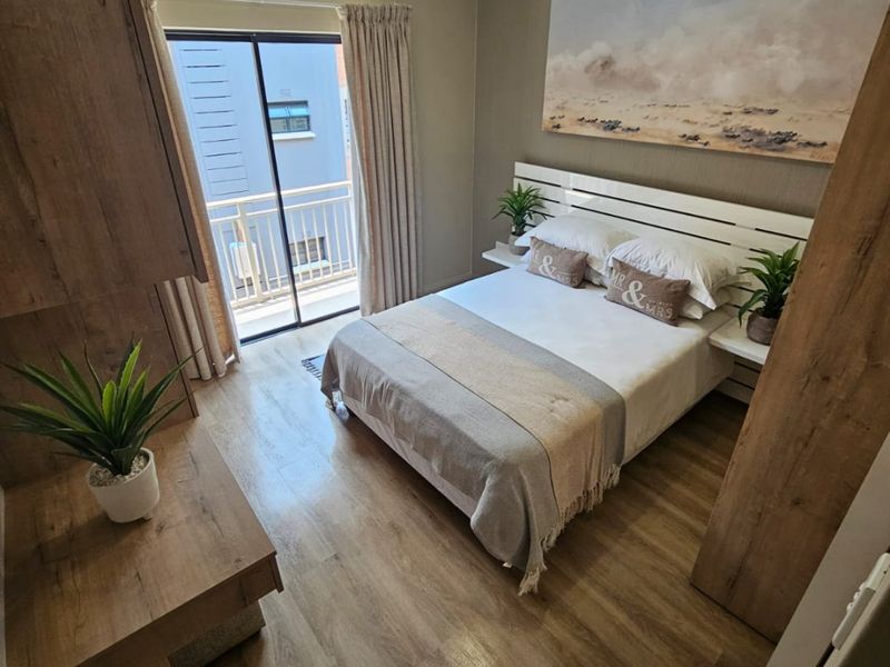 A well-maintained bedroom featuring laminate flooring, built-in cabinetry, and direct access to a private balcony through sliding glass doors.