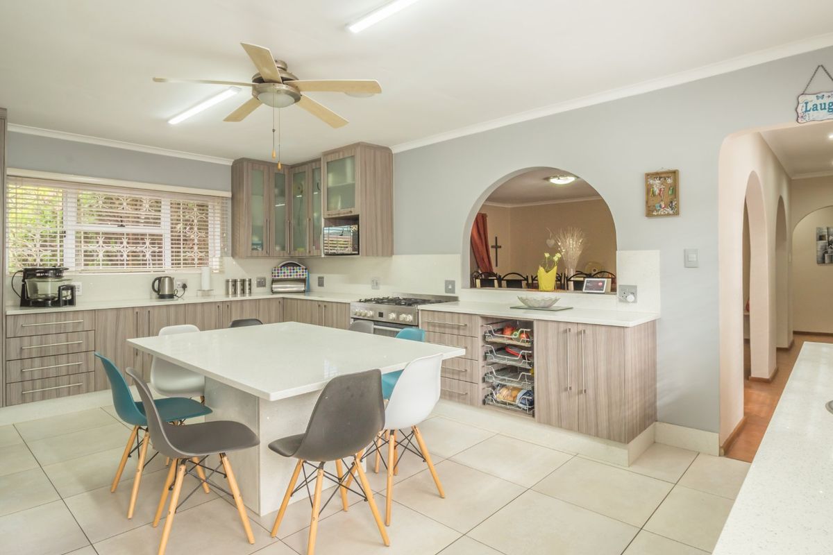 Spacious kitchen featuring modern wood-finish cabinetry, stone countertops, a central island, and a gas hob, with an open-plan layout connecting to adjacent living areas.