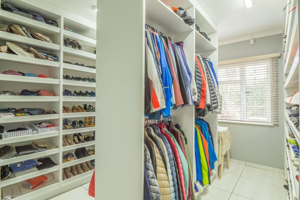 A well-organized walk-in closet featuring extensive built-in shelving and hanging space with bright tiled flooring and natural light from a window.