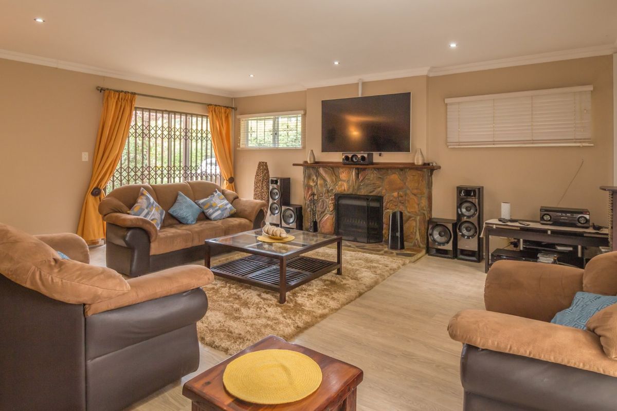 Spacious living room featuring a prominent stone fireplace, laminate flooring, and recessed lighting, offering a comfortable and functional family space.