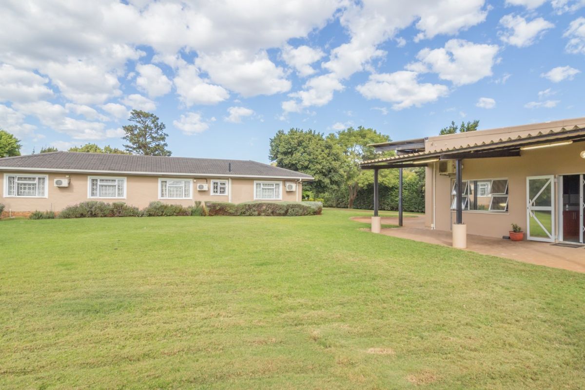 Spacious rear garden featuring a well-maintained lawn, a covered patio area, and exterior access to the main dwelling with integrated air conditioning units.