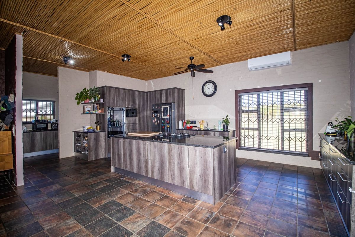 Spacious kitchen featuring a central island with granite countertops, built-in oven, gas hob, and a unique bamboo ceiling, offering a functional and rustic aesthetic.