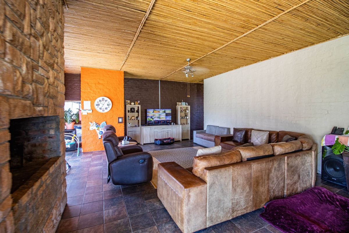 Spacious living room featuring a stone fireplace, unique thatched ceiling, and tiled flooring, offering a rustic and cozy atmosphere.