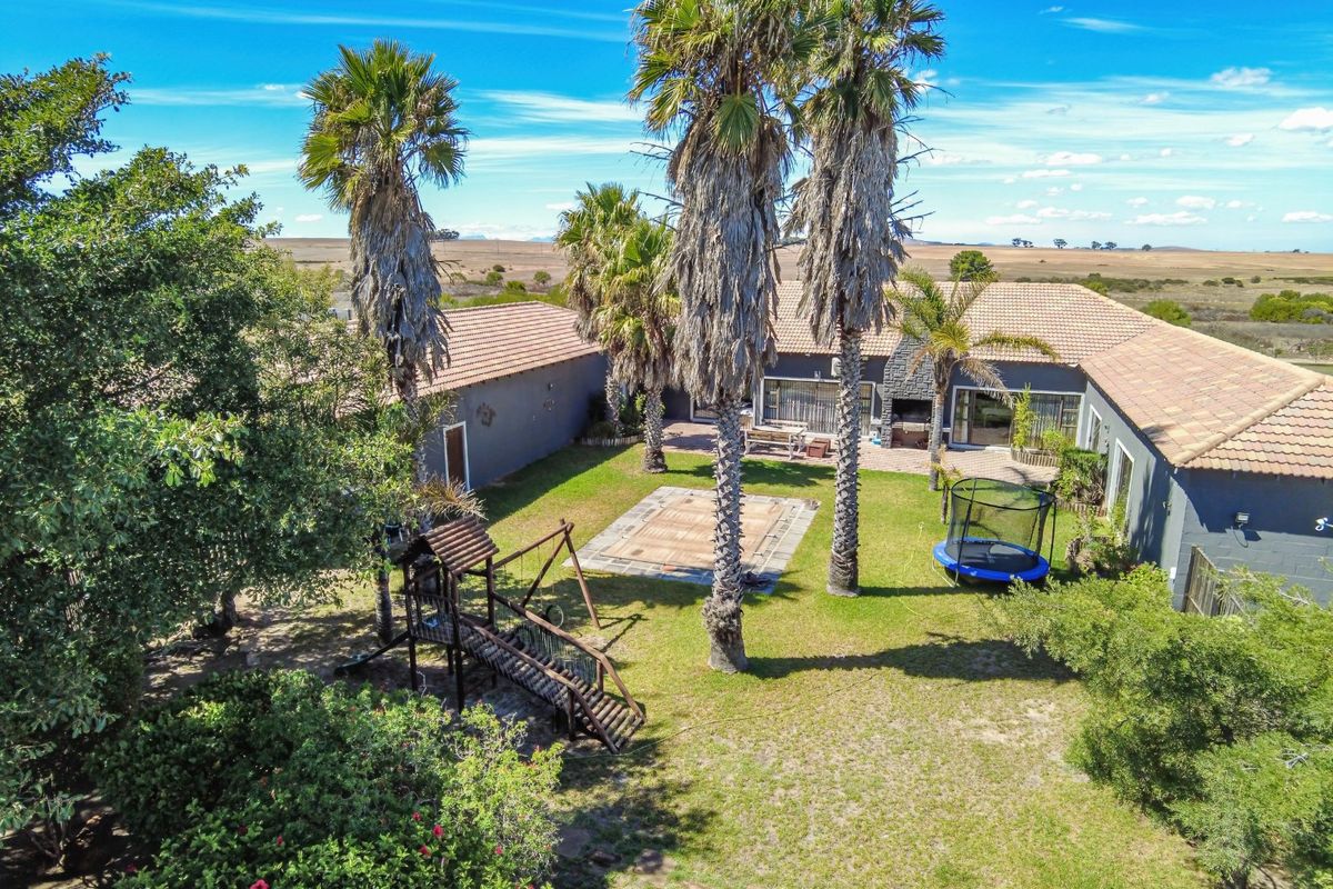 Aerial view of a spacious rear courtyard featuring a paved patio, built-in braai, and established garden set against a rural landscape.
