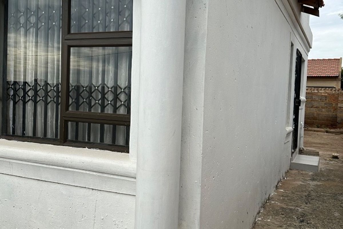 Side view of the property exterior featuring a decorative column, security gate, and paved walkway along the building perimeter.