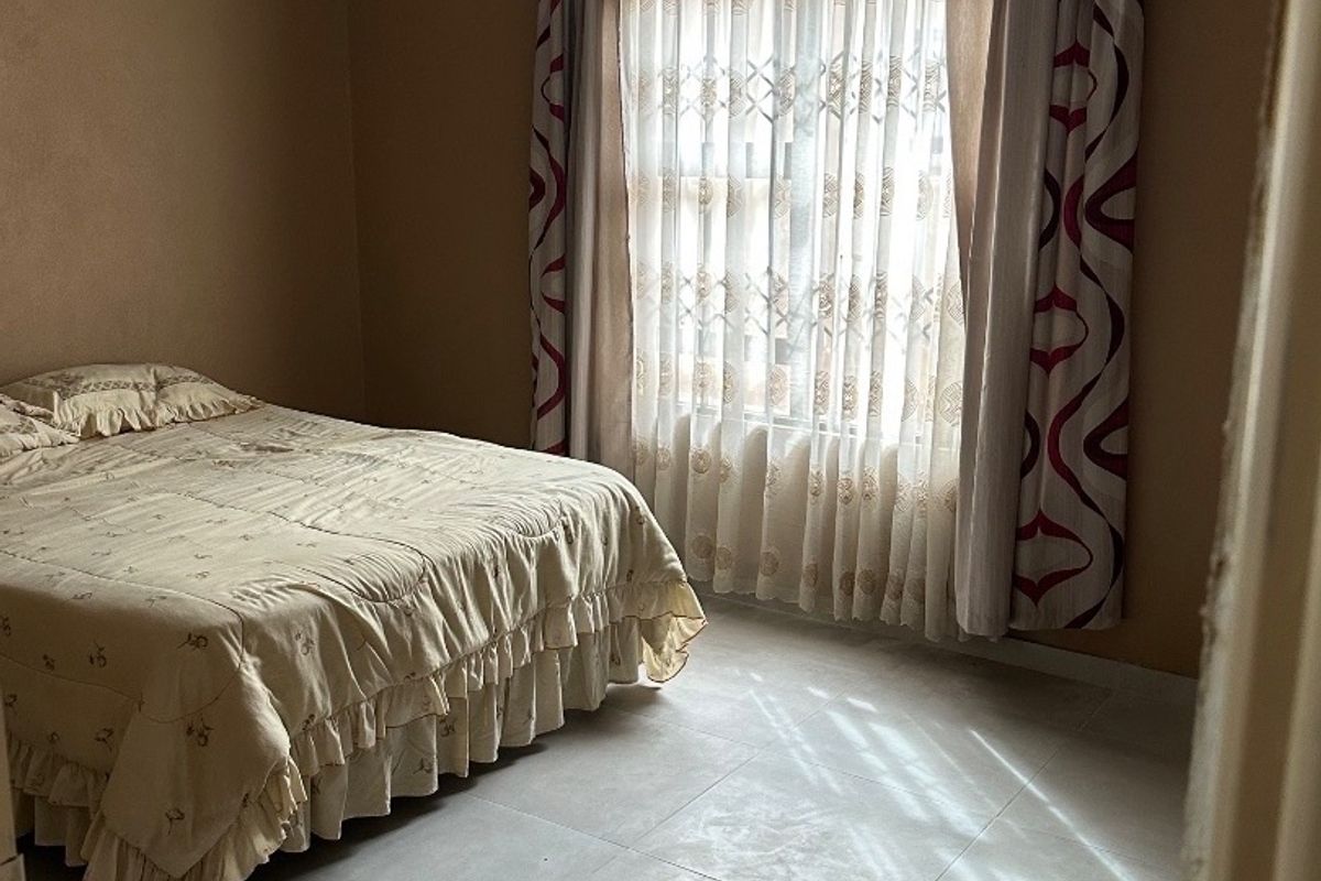 A bedroom featuring tiled flooring, a panelled ceiling with decorative cornice, and natural light through a window with curtains.