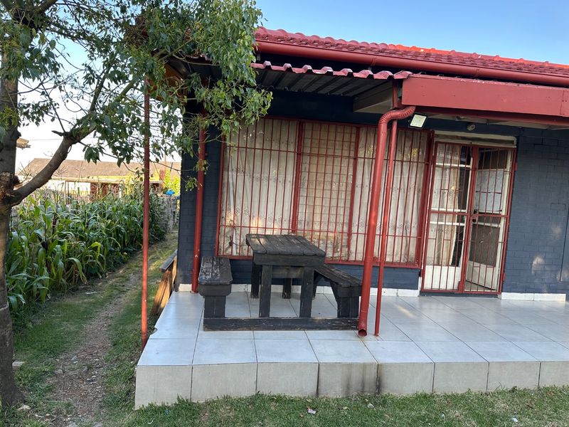 A covered patio area featuring tiled flooring, security bars on windows and doors, and a metal roof structure.