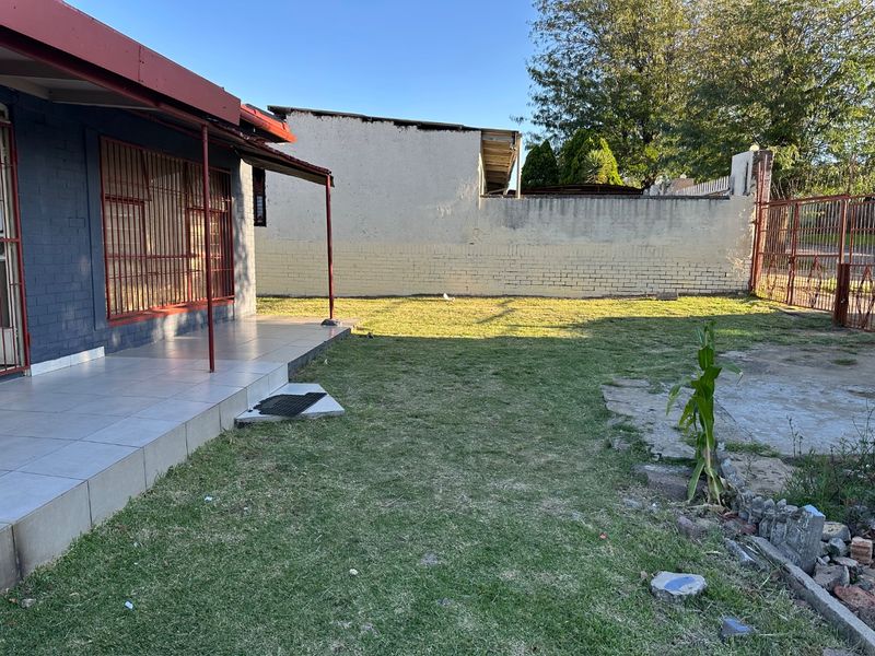 Rear exterior view featuring a tiled patio, lawn area, and perimeter boundary wall with metal security fencing.