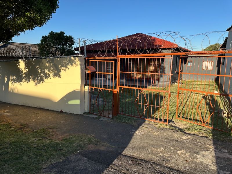 Front view of the property featuring a perimeter wall with razor wire security and a metal driveway gate.