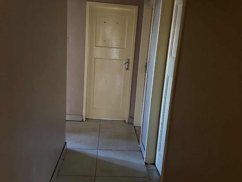 A narrow residential hallway featuring tiled flooring, multiple internal doors, and wall-mounted coat hooks, requiring minor cosmetic updates.