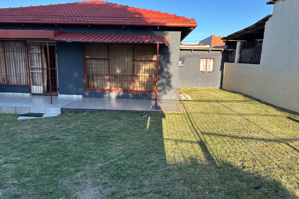 Rear view of the house featuring a tiled patio, security bars on windows, and a private garden area.