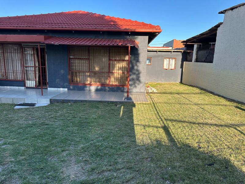Rear view of the house featuring a tiled patio, security bars on windows, and a private garden area.