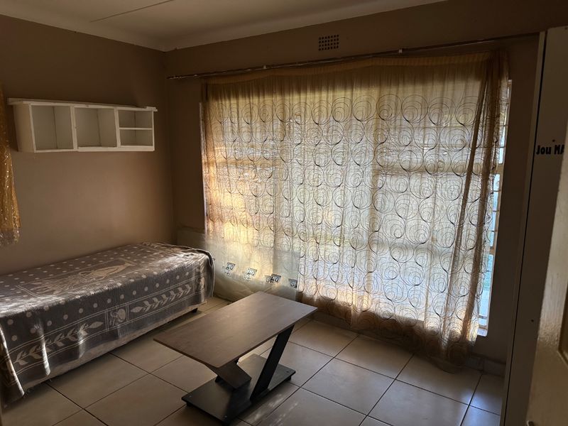 A bedroom featuring tiled flooring, built-in wall shelving, and a large window with security bars, offering a functional space with potential for cosmetic updates.