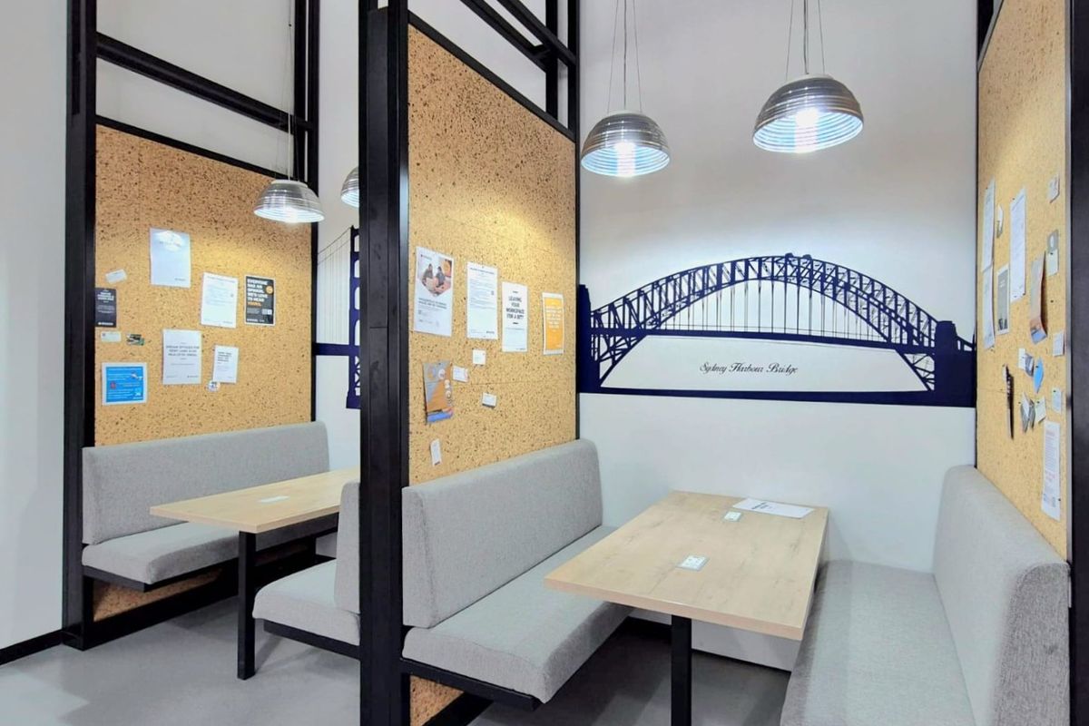 Modern commercial office space featuring partitioned booth seating areas with cork wall panels and contemporary pendant lighting.