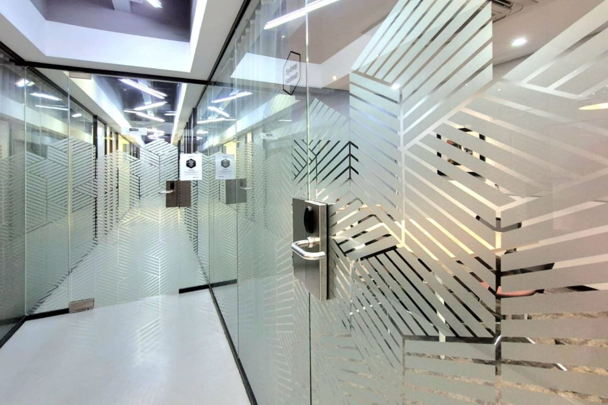 Modern commercial hallway featuring glass partition walls with decorative frosted film and recessed ceiling lighting.