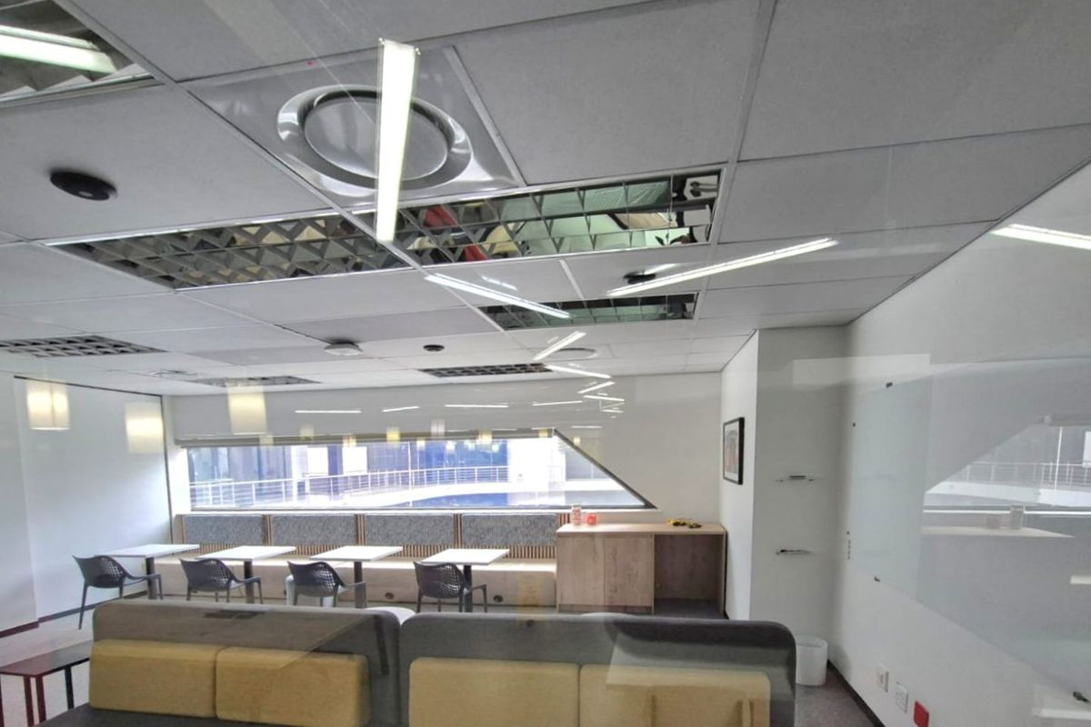 A modern commercial office space featuring a suspended ceiling, integrated bench seating, built-in cabinetry, and a whiteboard, suitable for collaborative work environments.