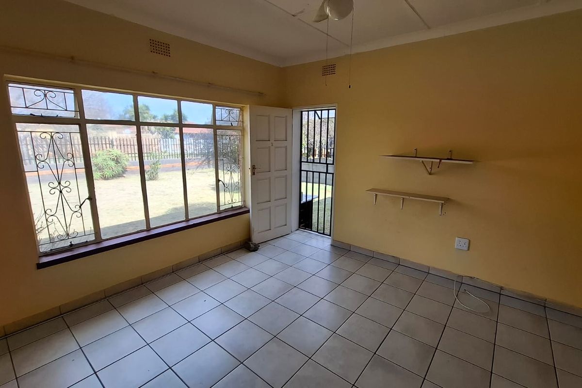 An empty living room featuring tiled flooring, a large window with security bars, and direct access to the garden through a security gate.