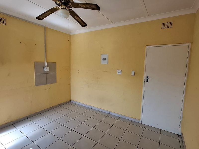 An empty bedroom featuring tiled flooring, a ceiling fan, and dated wall finishes, presenting a blank canvas for renovation or cosmetic updates.