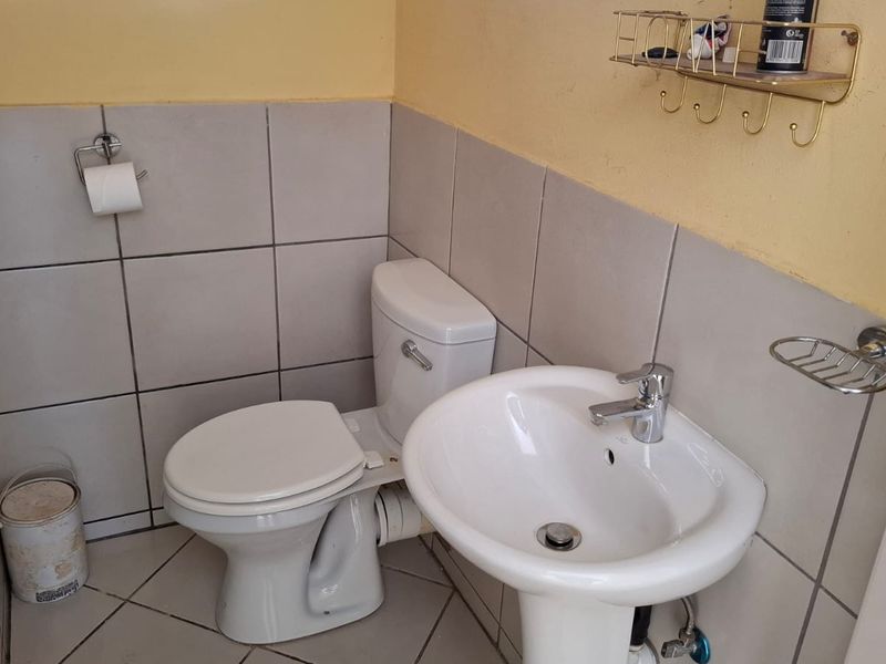 A compact bathroom featuring a pedestal basin, toilet, and neutral wall and floor tiling.