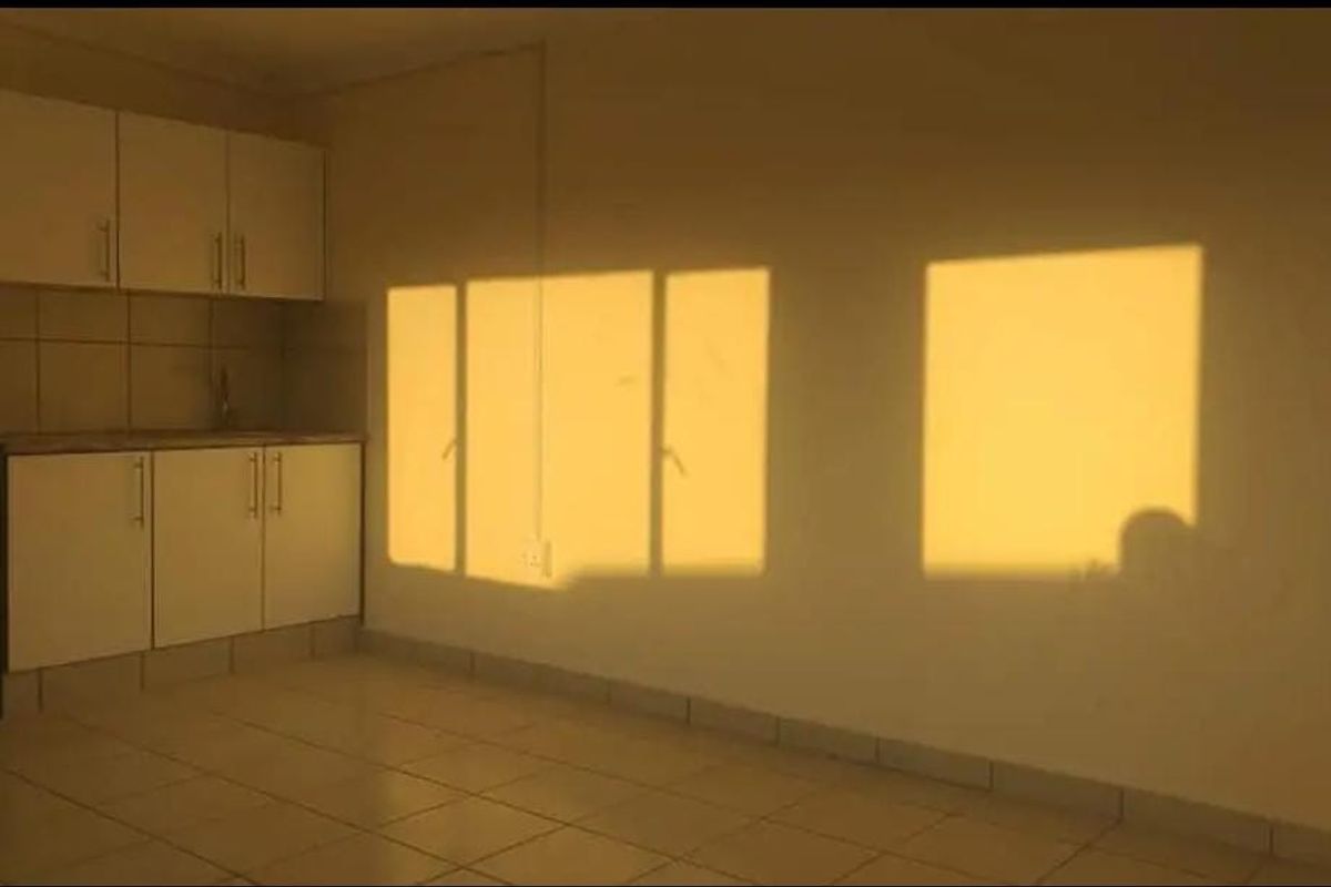 A compact, empty kitchen featuring built-in cabinetry, tiled flooring, and a tiled backsplash, illuminated by warm natural sunlight.
