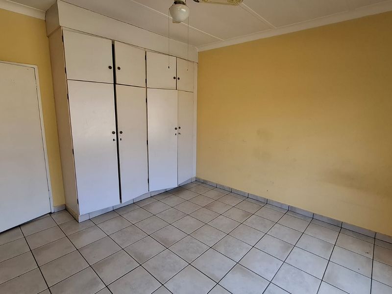 An empty bedroom featuring tiled flooring, built-in cupboards, and a ceiling fan, requiring cosmetic updates to the wall finishes.
