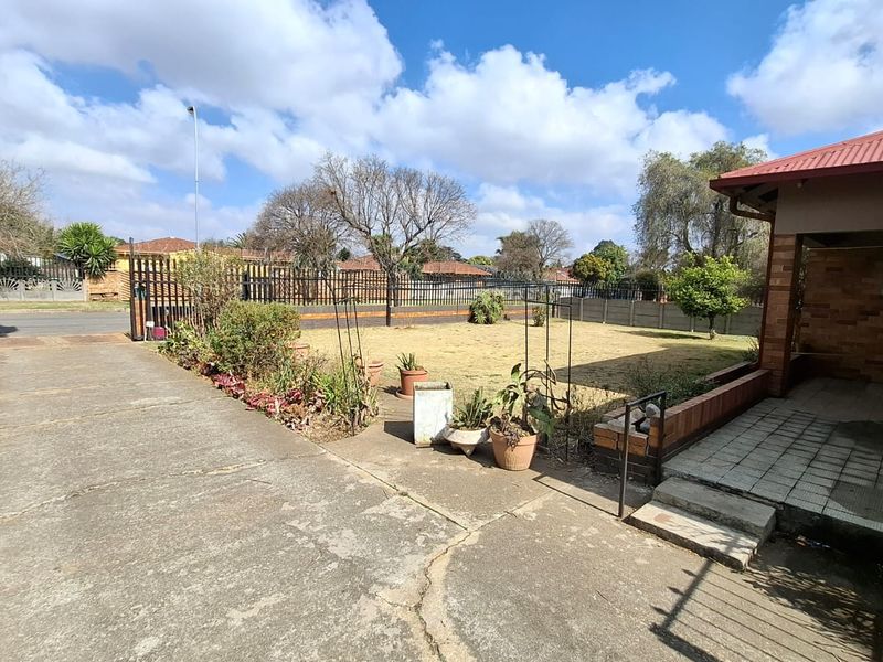 Front exterior view featuring a concrete driveway, brick facade, covered patio area, and perimeter fencing surrounding a lawn.