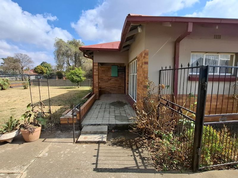 Front exterior view of a house featuring a brick facade, metal roof, paved walkway, and a wrought iron security gate.
