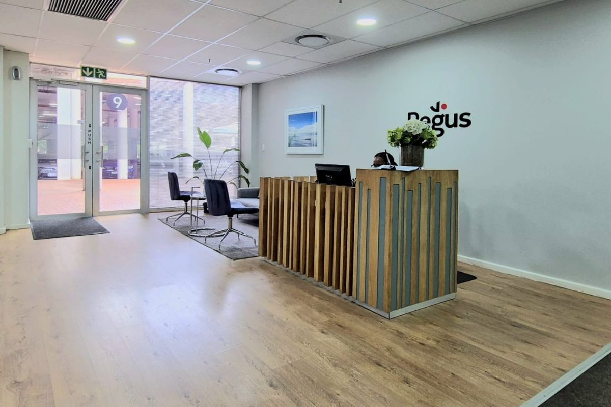 Professional commercial reception area featuring a modern wooden reception desk, wood-look flooring, recessed ceiling lighting, and glass entrance doors.