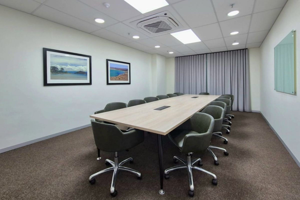 A professional commercial boardroom featuring a large central meeting table, recessed ceiling lighting, integrated air conditioning, and wall-mounted glass whiteboard.