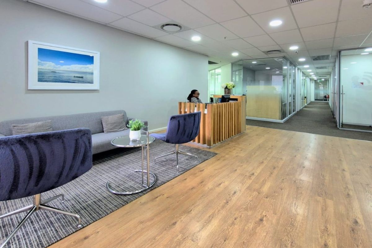 Modern commercial reception area featuring wood-look flooring, recessed ceiling lighting, and glass-partitioned office spaces.