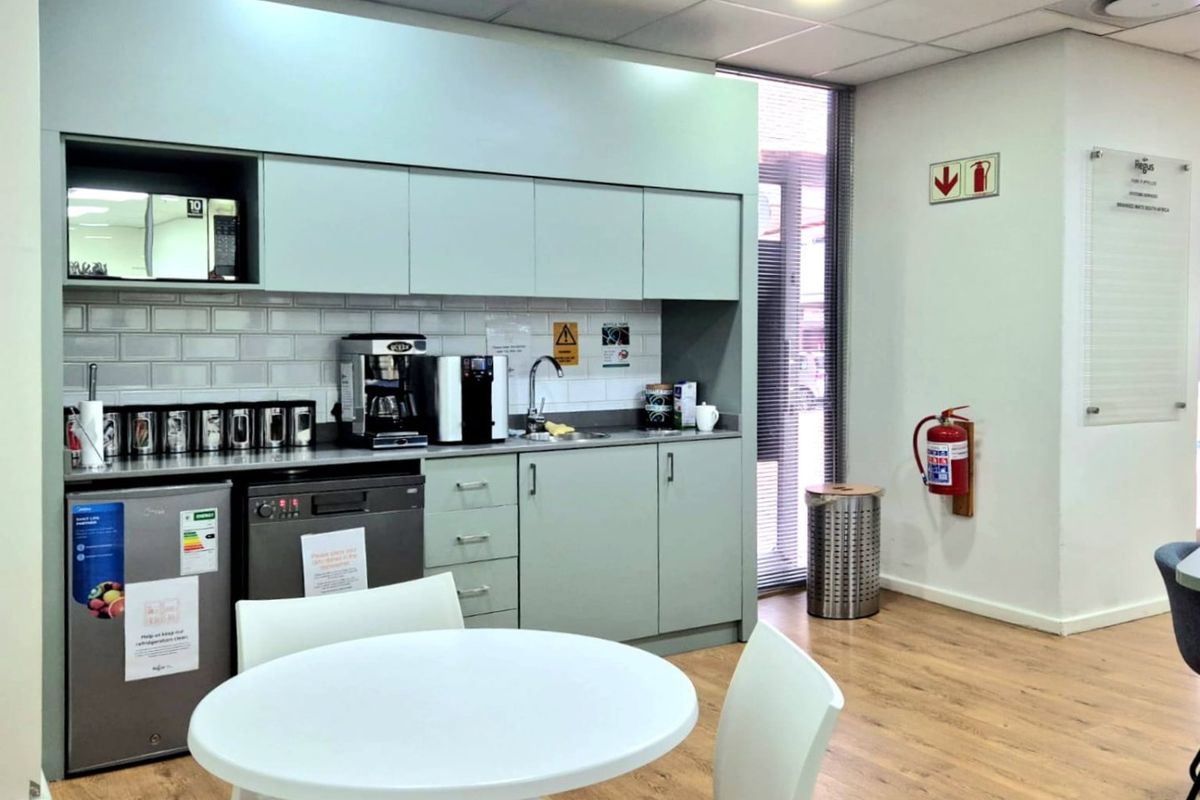 A clean, modern commercial kitchenette featuring built-in cabinetry, subway tile backsplash, integrated sink, and wood-look flooring in a professional office environment.