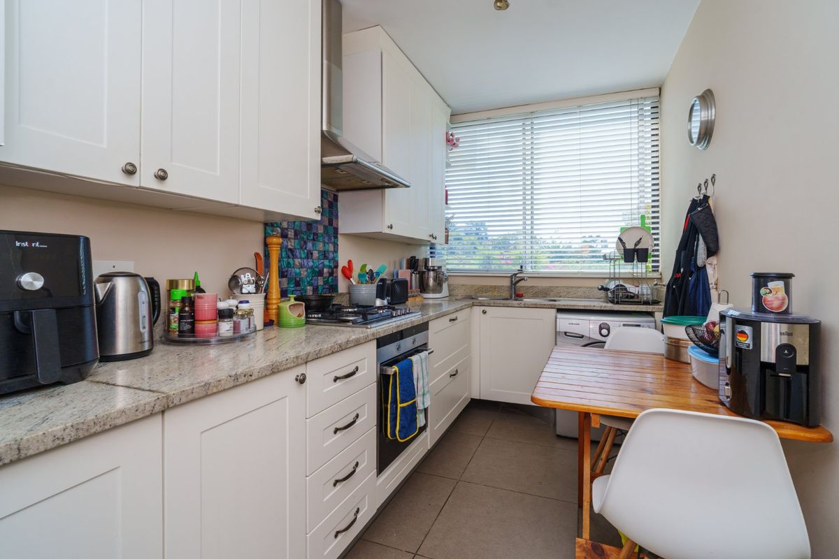 A functional galley-style kitchen featuring granite countertops, built-in cabinetry, a gas hob with extractor fan, and tiled flooring with natural light from the window.