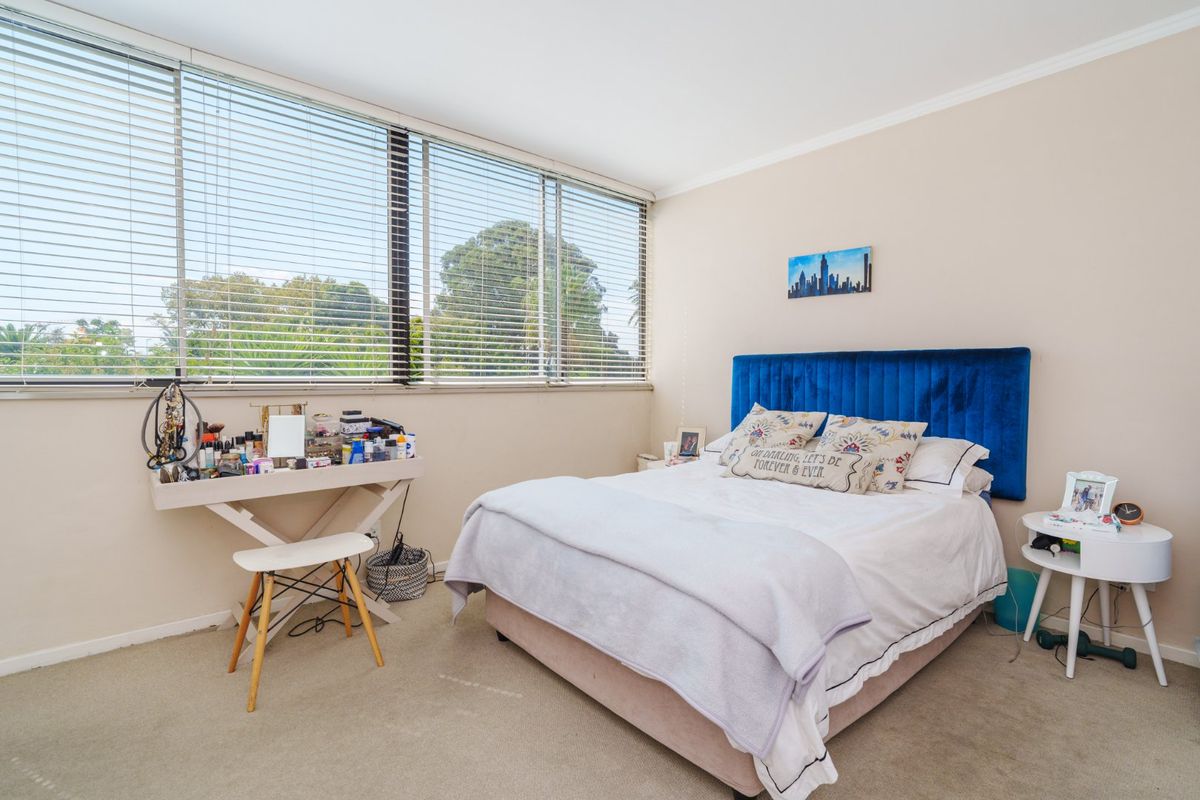A well-lit bedroom featuring large windows with venetian blinds and neutral carpeting, offering a comfortable and functional living space.