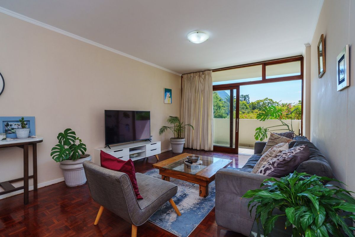 A comfortable living room featuring warm parquet flooring and a large sliding glass door that provides access to an outdoor balcony area.