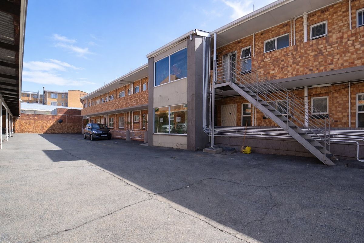 Exterior view of the apartment complex featuring brick facade, external metal staircase, and paved parking area.
