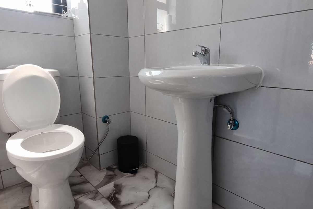 A clean, modern bathroom featuring a pedestal washbasin, toilet, and neutral grey wall tiling with marble-effect floor tiles.