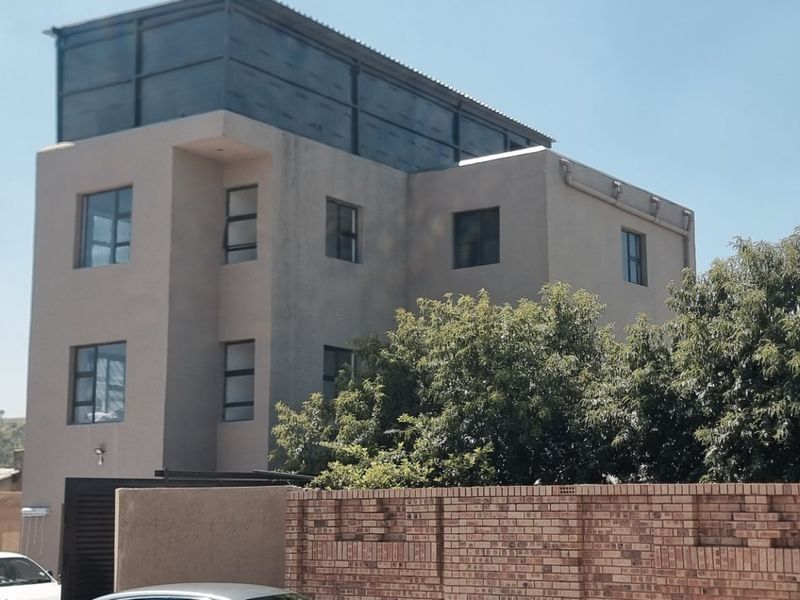 A multi-story residential building featuring a modern facade with aluminum windows, enclosed by a brick boundary wall.