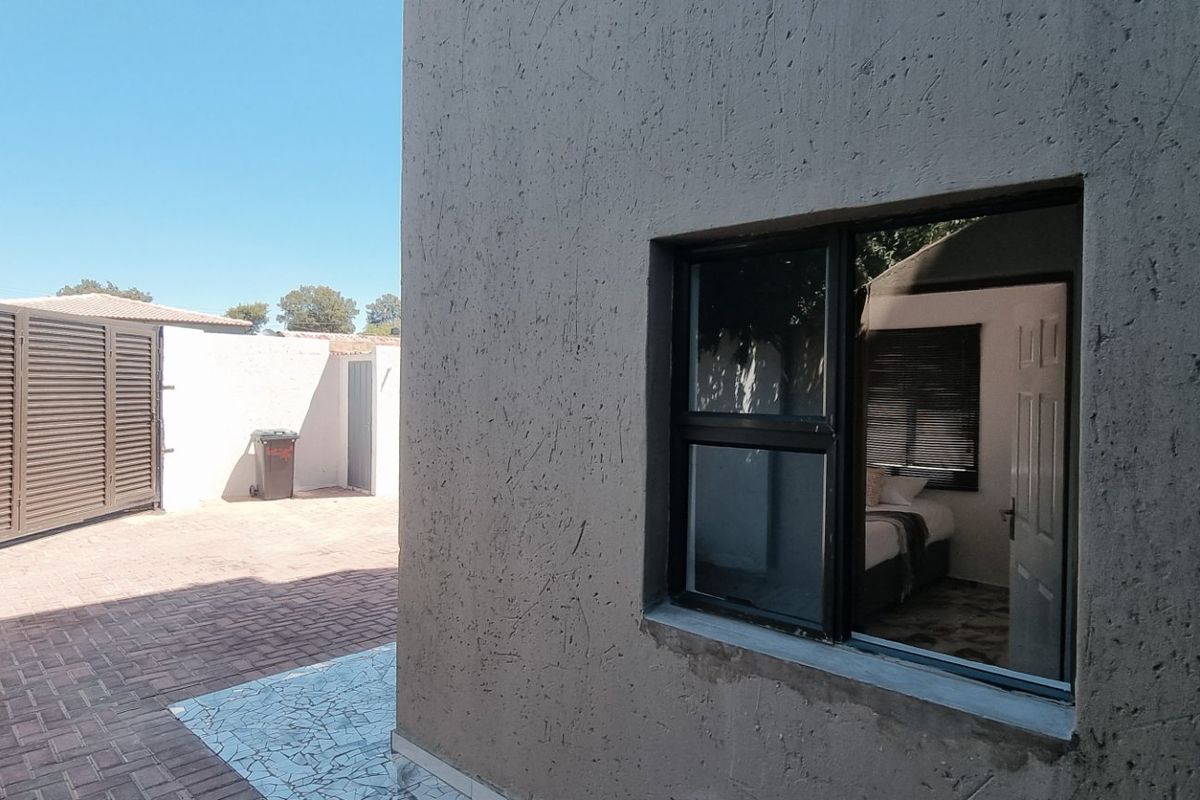 Rear exterior view showing a paved courtyard area, boundary wall, sliding gate, and an exterior wall with an aluminium window frame.