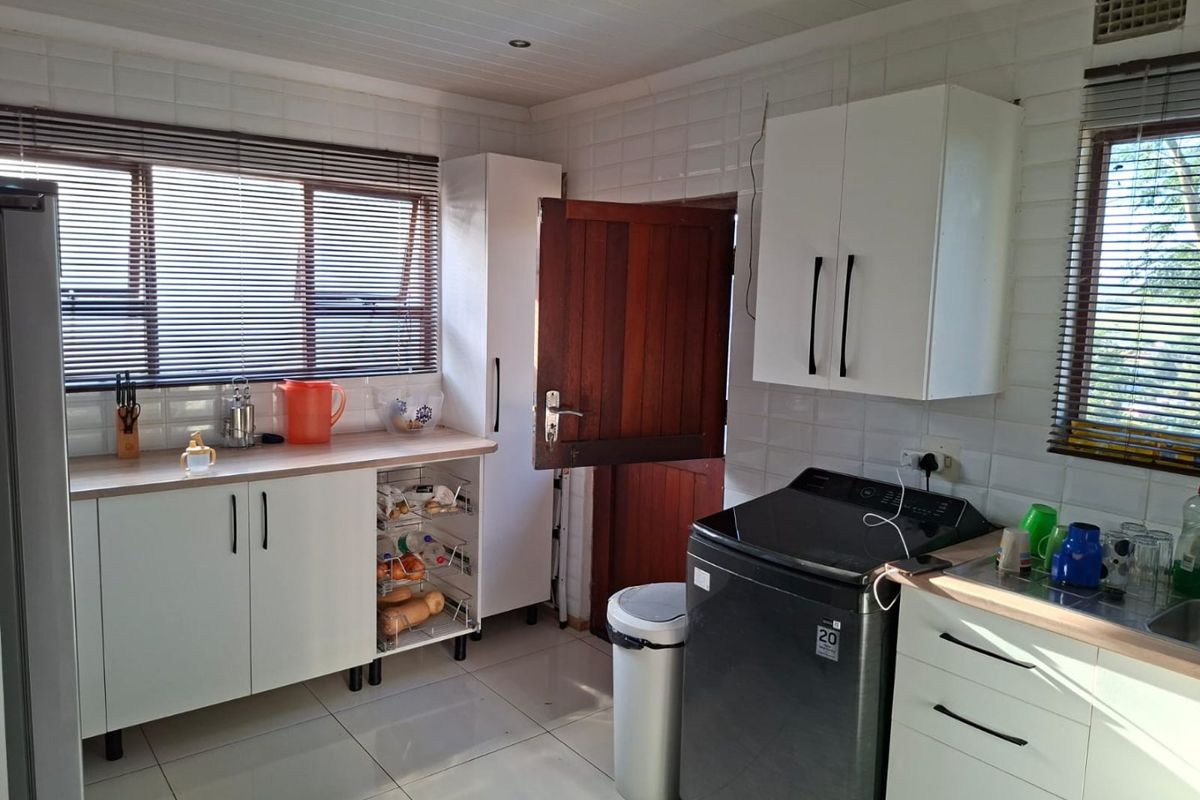 A functional kitchen featuring white cabinetry, laminate countertops, tiled splashbacks, and tiled flooring, with natural light provided by dual windows.