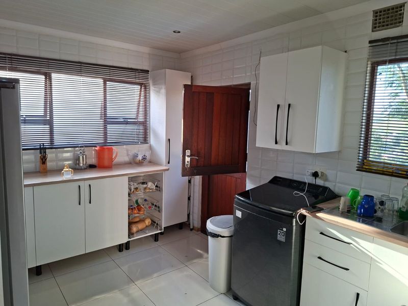A functional kitchen featuring white cabinetry, laminate countertops, tiled splashbacks, and tiled flooring, with natural light provided by dual windows.