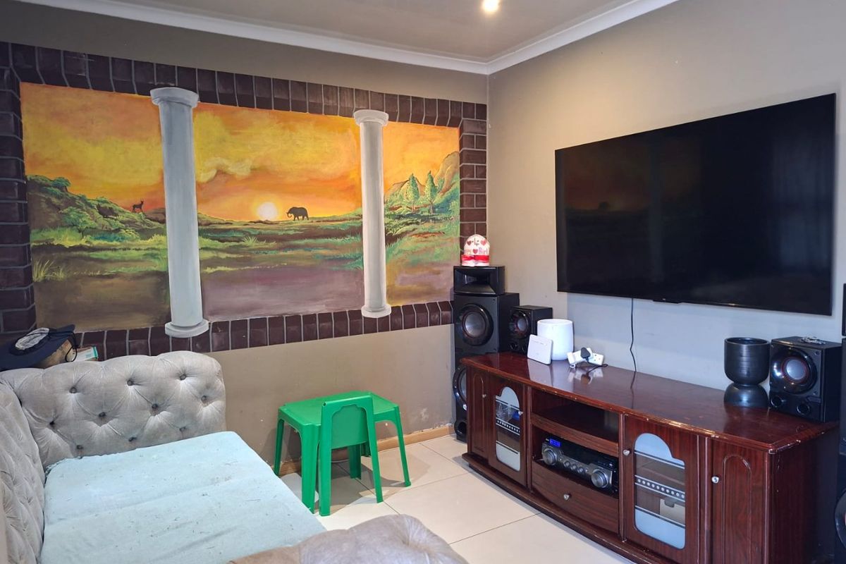 A living room featuring tiled flooring, recessed ceiling lighting, and a wall-mounted television, with a decorative mural on the feature wall.