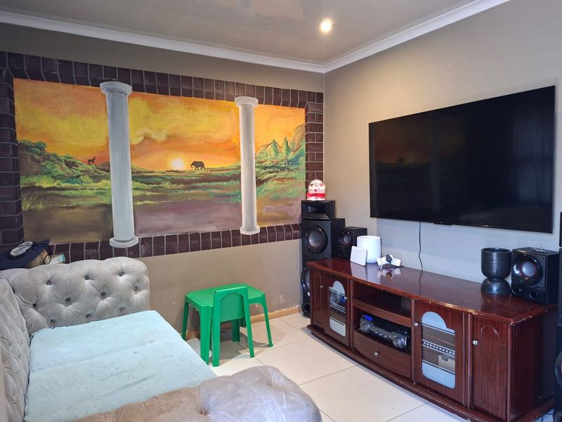 A living room featuring tiled flooring, recessed ceiling lighting, and a wall-mounted television, with a decorative mural on the feature wall.