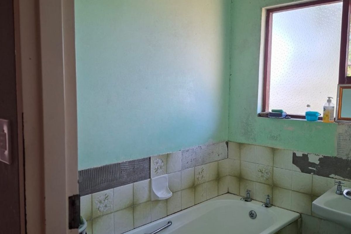 A dated bathroom featuring a standard bathtub and wall-mounted basin, requiring significant cosmetic updates and repairs to wall finishes and tiling.