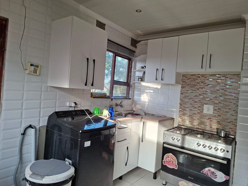 Compact kitchen featuring white cabinetry, a gas stove with oven, tiled backsplash, and integrated laundry plumbing connections.