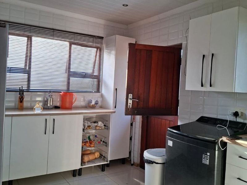 Functional laundry room featuring tiled flooring, white cabinetry, tiled splashbacks, and a timber door with access to the exterior.