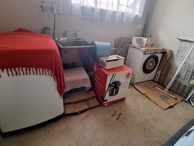 A functional laundry area featuring a stainless steel sink and concrete flooring, requiring some maintenance and organization.
